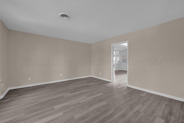 spare room with dark wood-style flooring, visible vents, baseboards, and a textured ceiling