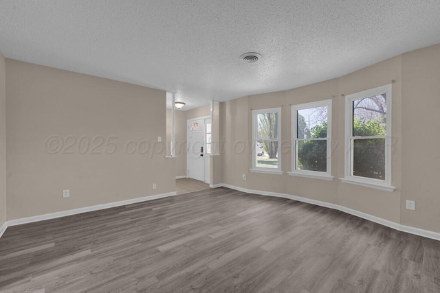 unfurnished room featuring a textured ceiling, wood finished floors, visible vents, and a healthy amount of sunlight