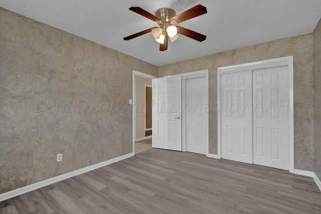 unfurnished bedroom with baseboards, ceiling fan, two closets, and wood finished floors