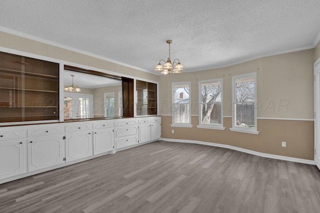 unfurnished dining area featuring light wood-style flooring, a textured ceiling, an inviting chandelier, and ornamental molding