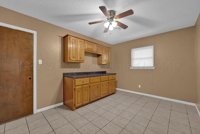 kitchen with a textured ceiling, light tile patterned flooring, dark countertops, and a ceiling fan