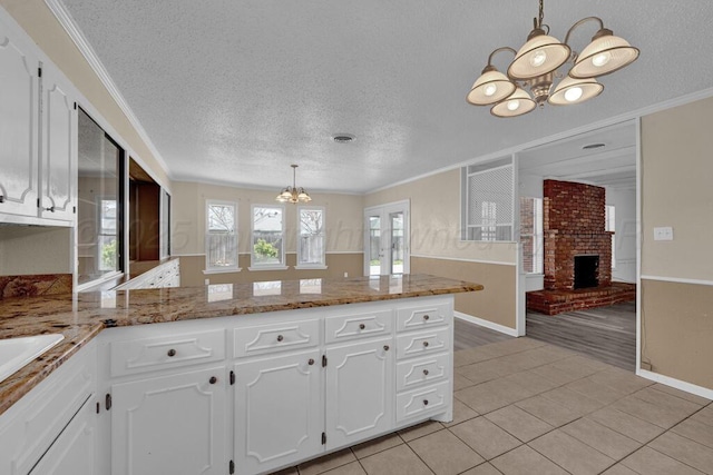 kitchen with light tile patterned floors, a peninsula, a textured ceiling, white cabinets, and a notable chandelier