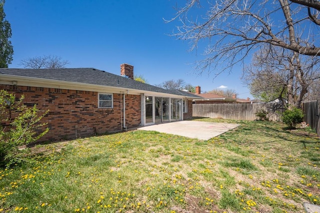 rear view of house with a fenced backyard, a lawn, a patio area, brick siding, and a chimney