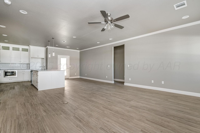 unfurnished living room featuring ceiling fan, ornamental molding, and wood-type flooring