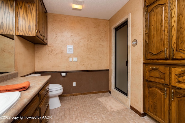 bathroom with vanity, toilet, a textured ceiling, and a shower with shower door