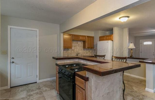 kitchen with white refrigerator, backsplash, gas stove, and a breakfast bar area