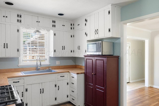 kitchen with a sink, stainless steel microwave, light countertops, ornamental molding, and white cabinetry