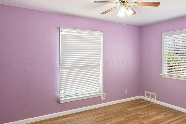 empty room with wood finished floors, plenty of natural light, ceiling fan, and baseboards