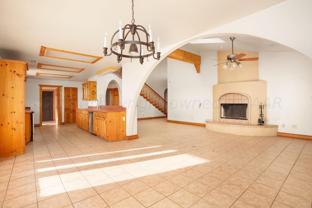 kitchen with ceiling fan with notable chandelier, light tile patterned floors, stainless steel dishwasher, a tile fireplace, and vaulted ceiling