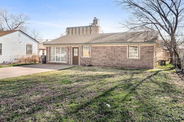 view of front of home with brick siding, roof with shingles, a front yard, and fence