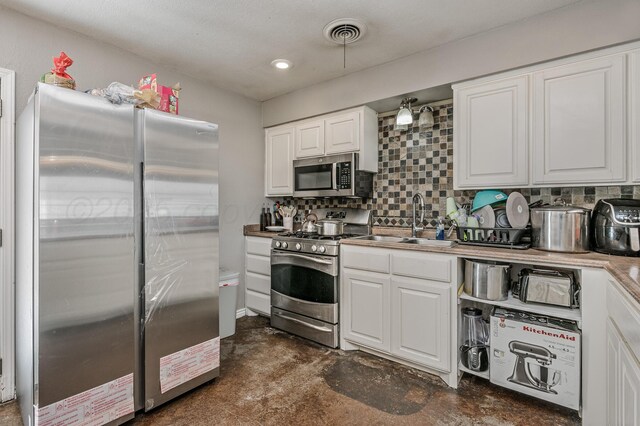 kitchen featuring visible vents, backsplash, appliances with stainless steel finishes, white cabinets, and a sink