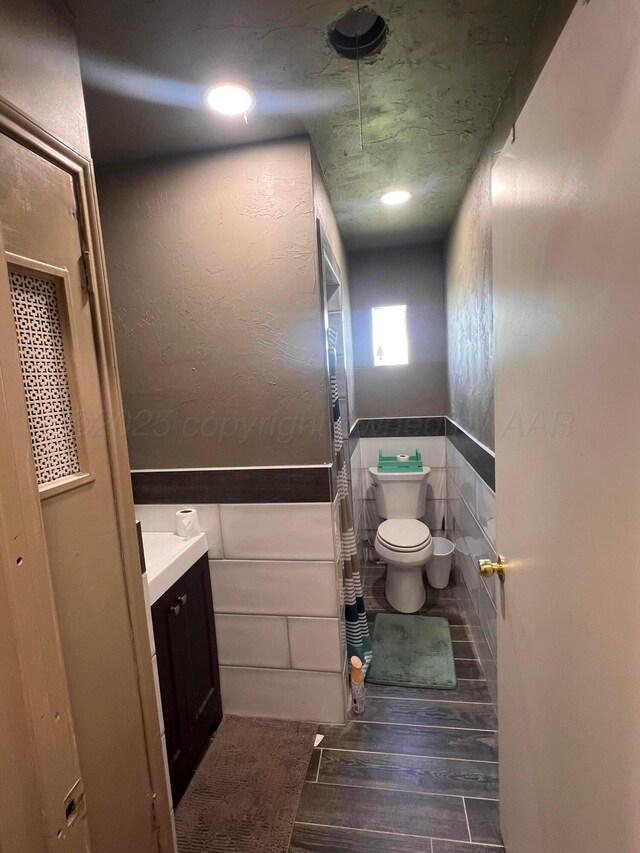 434 Long St, Hereford, TX 79045 - bathroom with wood finished floors, toilet, vanity, wainscoting, and tile walls