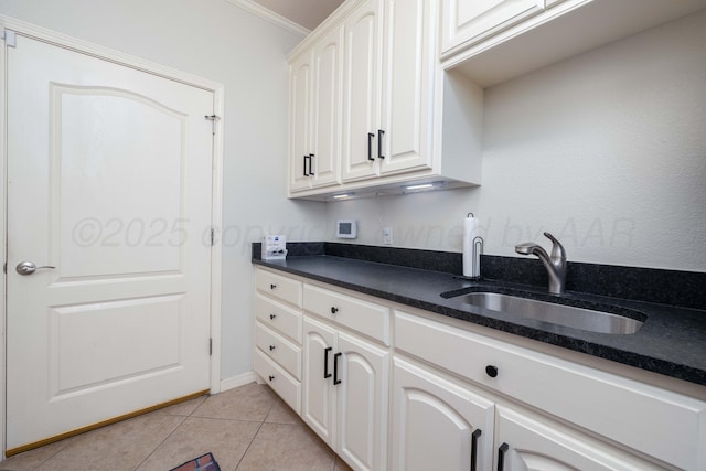 kitchen featuring crown molding, white cabinetry, a sink, dark stone countertops, and light tile patterned floors