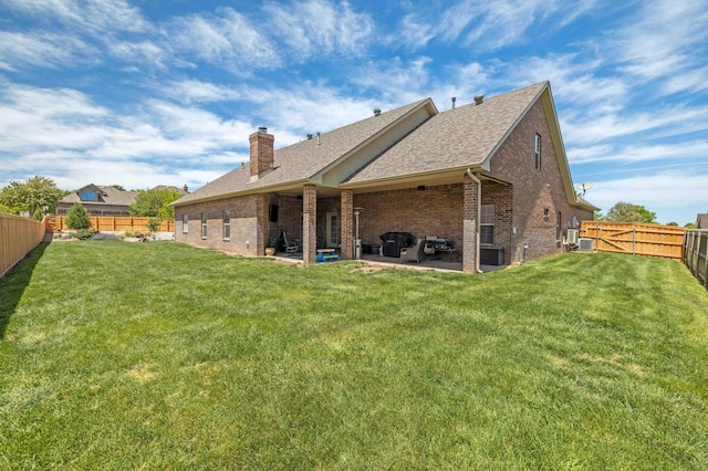 back of house featuring a chimney, a lawn, a patio area, brick siding, and a fenced backyard