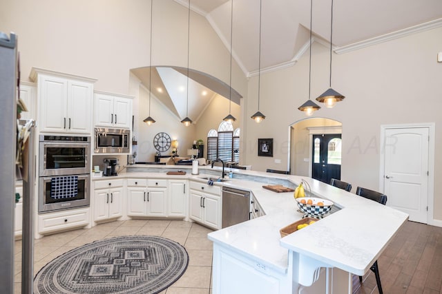 kitchen featuring high vaulted ceiling, ornamental molding, stainless steel appliances, and a kitchen bar