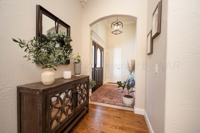 doorway to outside with wood-type flooring, arched walkways, baseboards, and an inviting chandelier