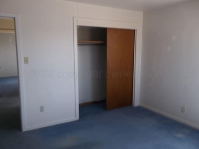 unfurnished bedroom with dark colored carpet and a closet