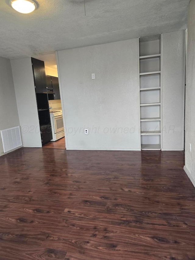 empty room featuring built in features, dark hardwood / wood-style floors, and a textured ceiling