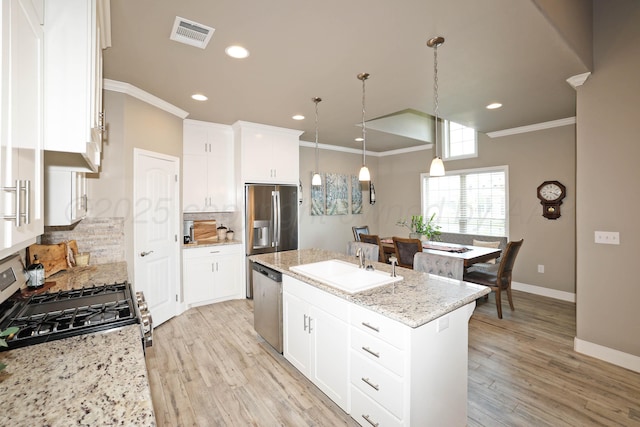 6702 Tatum Cir, Amarillo, TX 79119 - kitchen featuring appliances with stainless steel finishes, a kitchen island with sink, tasteful backsplash, light wood finished floors, and ornamental molding