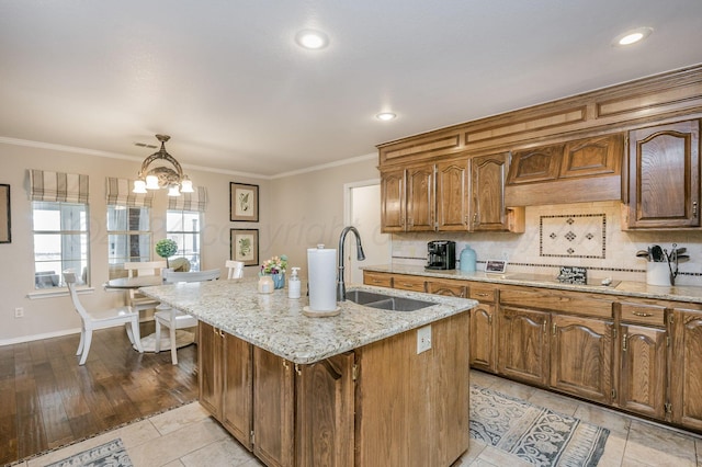 kitchen featuring hanging light fixtures, cooktop, a chandelier, light hardwood / wood-style floors, and a center island with sink