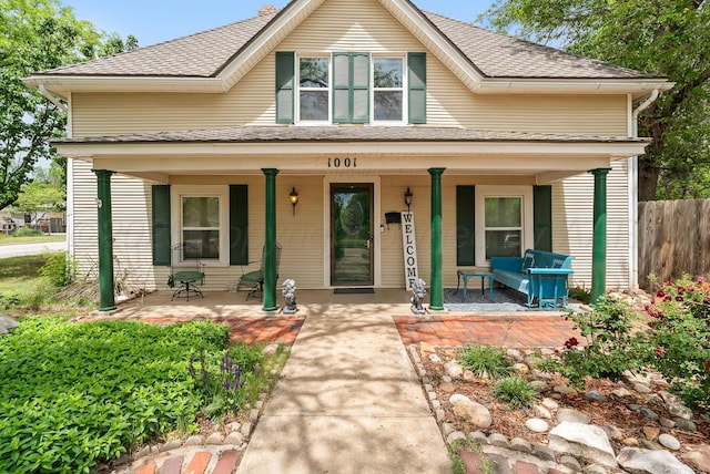 bungalow with a shingled roof, covered porch, and fence