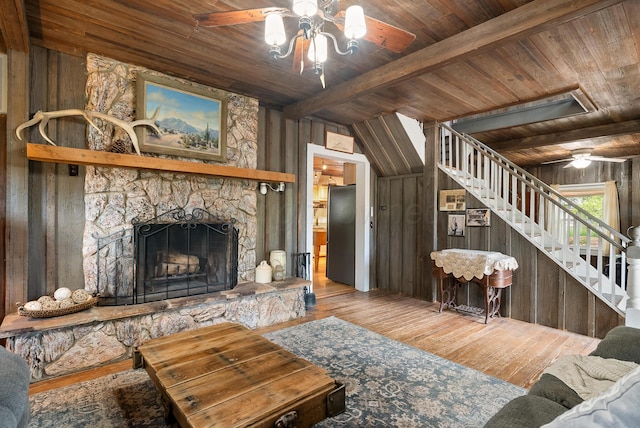 living room featuring wood walls, wood finished floors, stairway, ceiling fan, and wood ceiling
