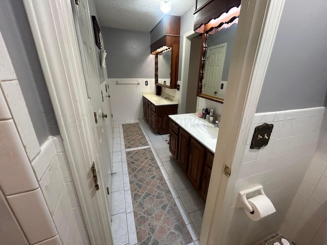 7906 Merchant Dr, Amarillo, TX 79121 - bathroom featuring two vanities, tile walls, wainscoting, and a textured ceiling