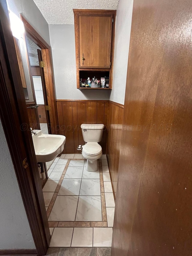 7906 Merchant Dr, Amarillo, TX 79121 - bathroom featuring wood walls, a wainscoted wall, toilet, a sink, and a textured ceiling