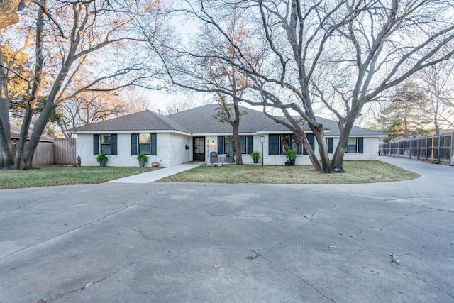 ranch-style home with driveway, a shingled roof, fence, and a front yard