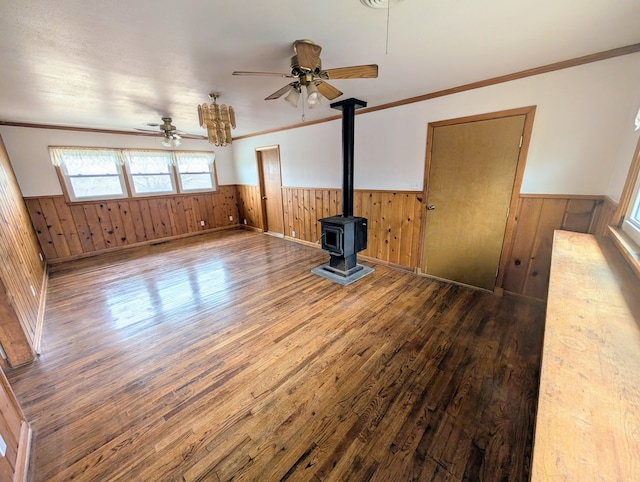 unfurnished living room with hardwood / wood-style flooring, ceiling fan, wood walls, ornamental molding, and a wood stove