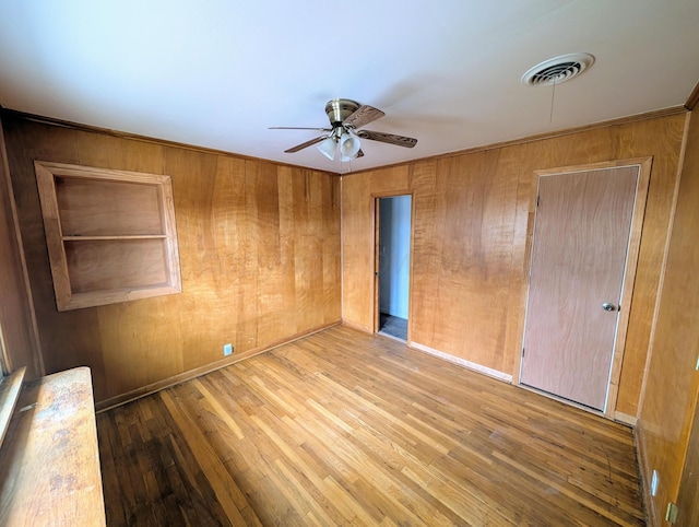 unfurnished bedroom with wooden walls, ceiling fan, and light hardwood / wood-style flooring