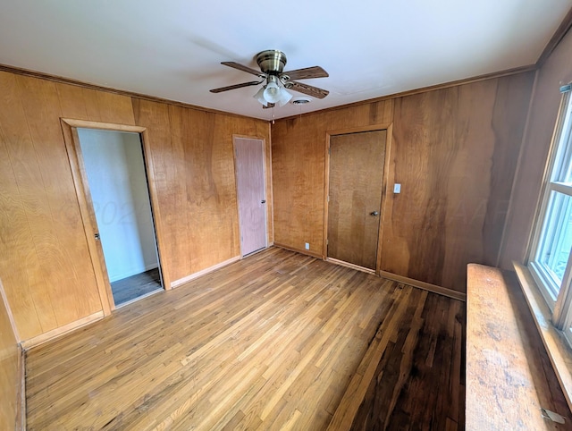 unfurnished bedroom with light hardwood / wood-style flooring, a closet, ceiling fan, wooden walls, and ornamental molding