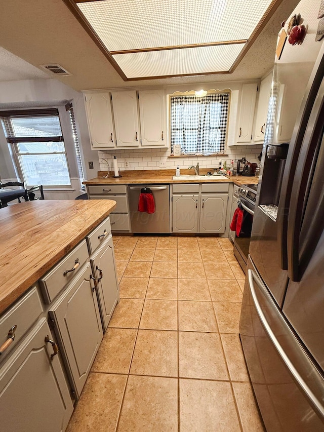 kitchen featuring decorative backsplash, butcher block counters, light tile patterned floors, and stainless steel appliances