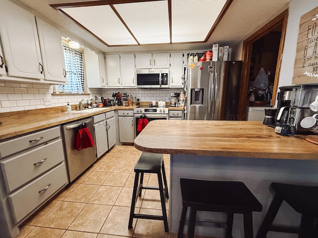 kitchen with tasteful backsplash, wooden counters, light tile patterned floors, stainless steel appliances, and a sink