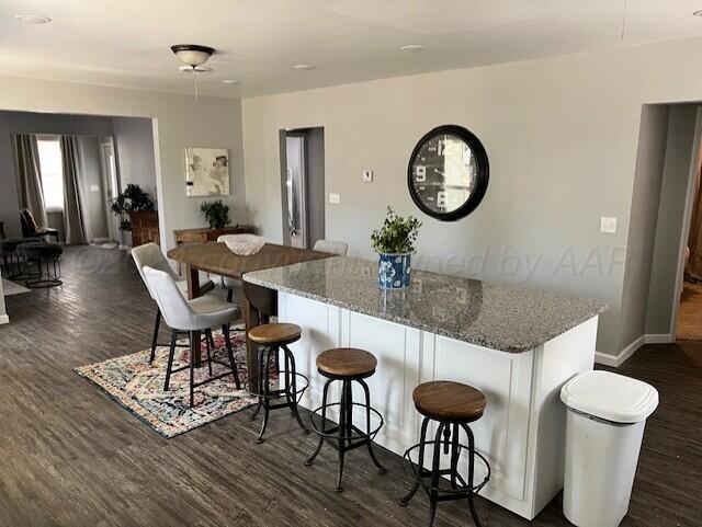 823 S Palo Duro St, Amarillo, TX 79106 - kitchen with dark wood-style floors, a kitchen island, stone counters, a kitchen breakfast bar, and baseboards
