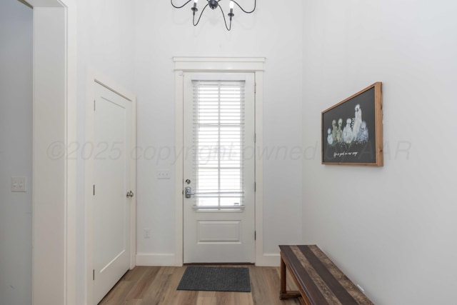 doorway to outside with a healthy amount of sunlight, light wood-type flooring, a notable chandelier, and baseboards