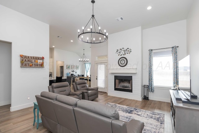 living room with recessed lighting, an inviting chandelier, light wood-style flooring, a brick fireplace, and visible vents
