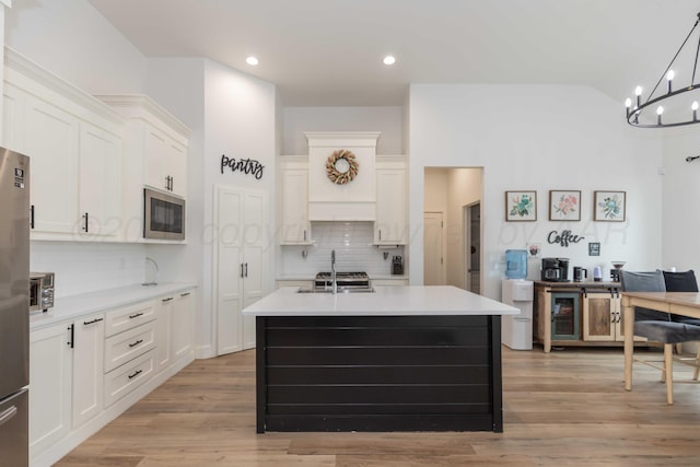 kitchen featuring stainless steel microwave, white cabinetry, decorative backsplash, light countertops, and an island with sink