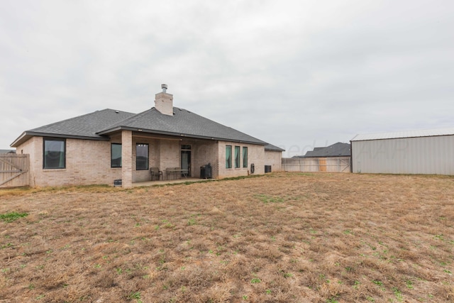 back of property with a patio area, a chimney, brick siding, roof with shingles, and fence