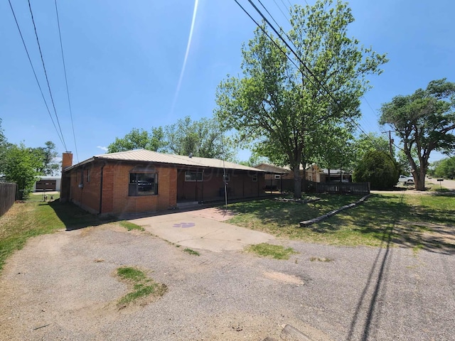 view of front of property with metal roof, brick siding, a front yard, and fence