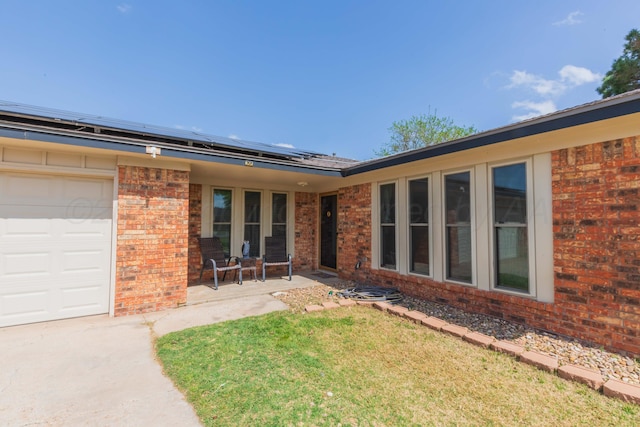 back of property featuring brick siding, roof mounted solar panels, a lawn, and a garage