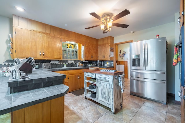 kitchen with light tile patterned flooring, sink, stainless steel fridge with ice dispenser, tile counters, and backsplash