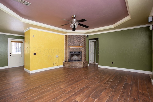 unfurnished living room with crown molding, a brick fireplace, dark hardwood / wood-style flooring, a raised ceiling, and ceiling fan