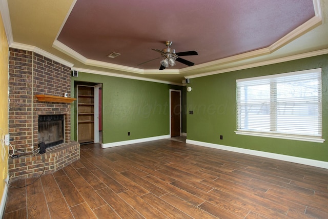 unfurnished living room featuring ornamental molding, ceiling fan, a tray ceiling, a brick fireplace, and dark wood-type flooring