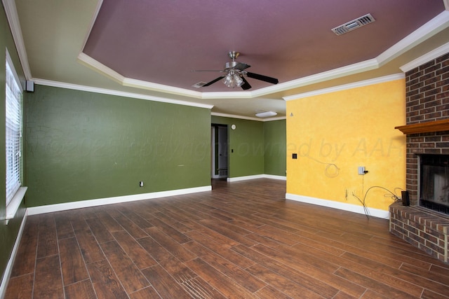 unfurnished living room with dark hardwood / wood-style flooring, ceiling fan, a tray ceiling, crown molding, and a brick fireplace