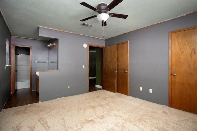 unfurnished bedroom with ceiling fan, dark carpet, and ensuite bath