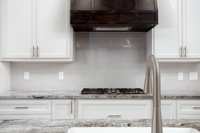 kitchen with decorative backsplash, under cabinet range hood, and white cabinetry