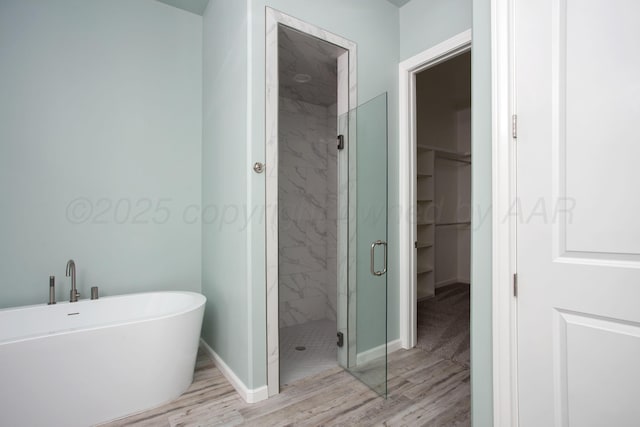 bathroom with a shower stall, a spacious closet, baseboards, and wood finished floors