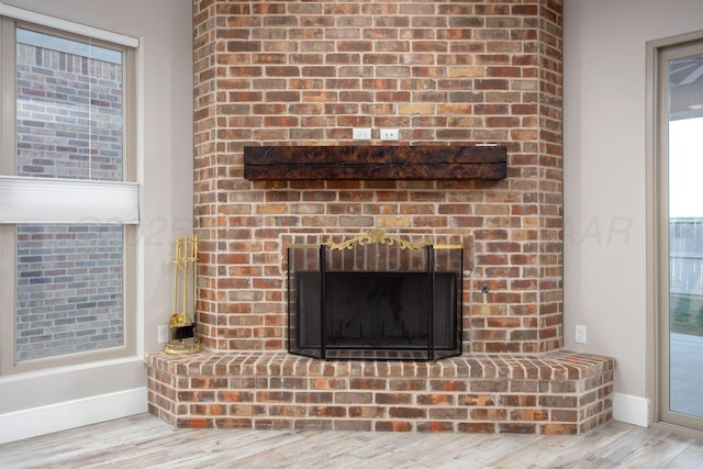 interior details with wood finished floors, a brick fireplace, and baseboards