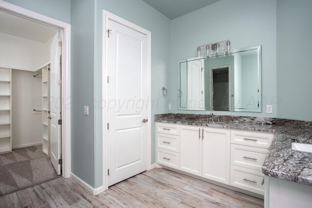 bathroom featuring baseboards, wood finished floors, vanity, and a spacious closet